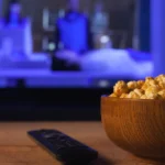 Bol de pop-corn et télécommande devant une télévision allumée le soir
