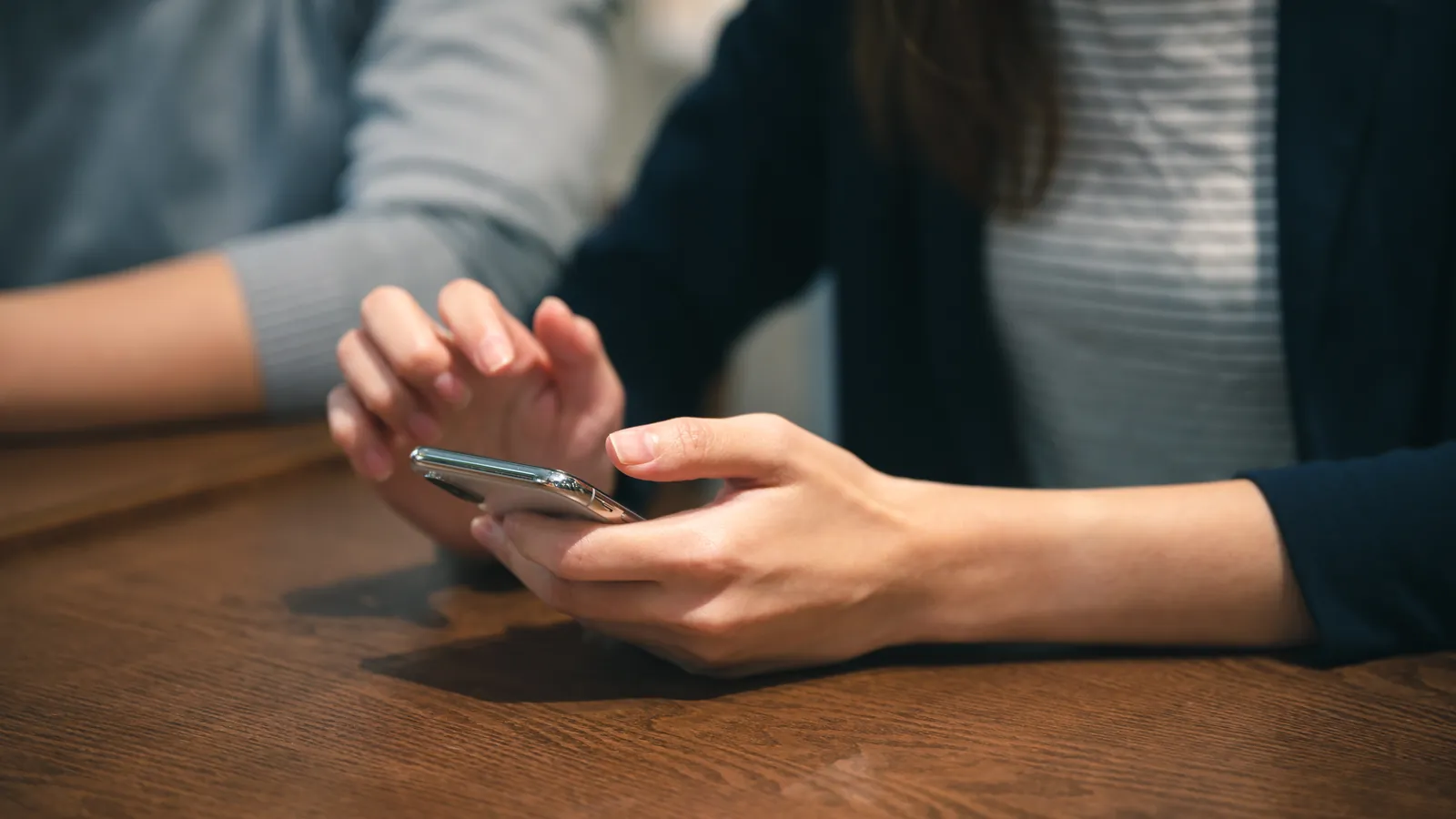 Personne utilisant un smartphone à deux mains sur une table en bois