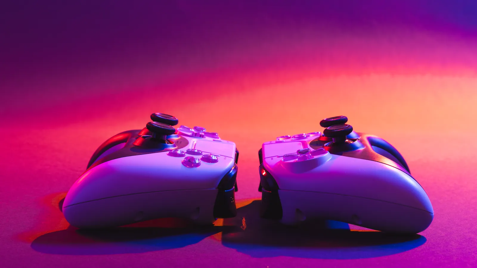 Deux manettes de jeu vidéo blanches sous un éclairage néon rose et violet