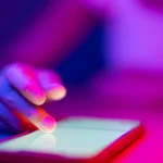 Doigt touchant l'écran d'un smartphone sous un éclairage néon rose et bleu