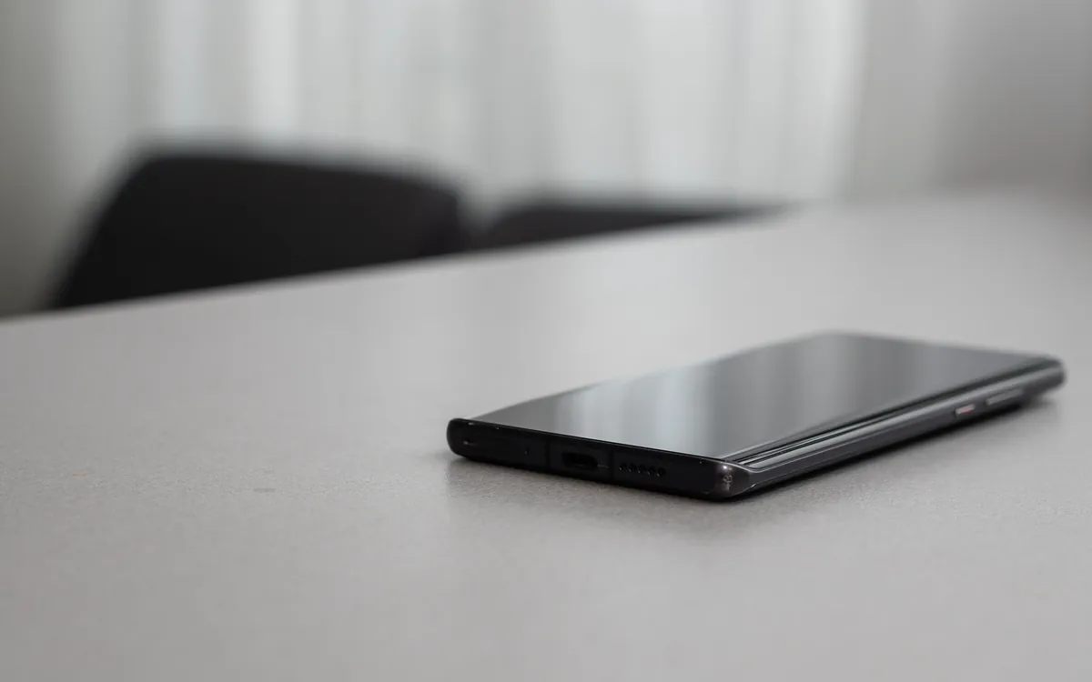 Smartphone noir posé à plat sur un bureau blanc, dans une lumière douce