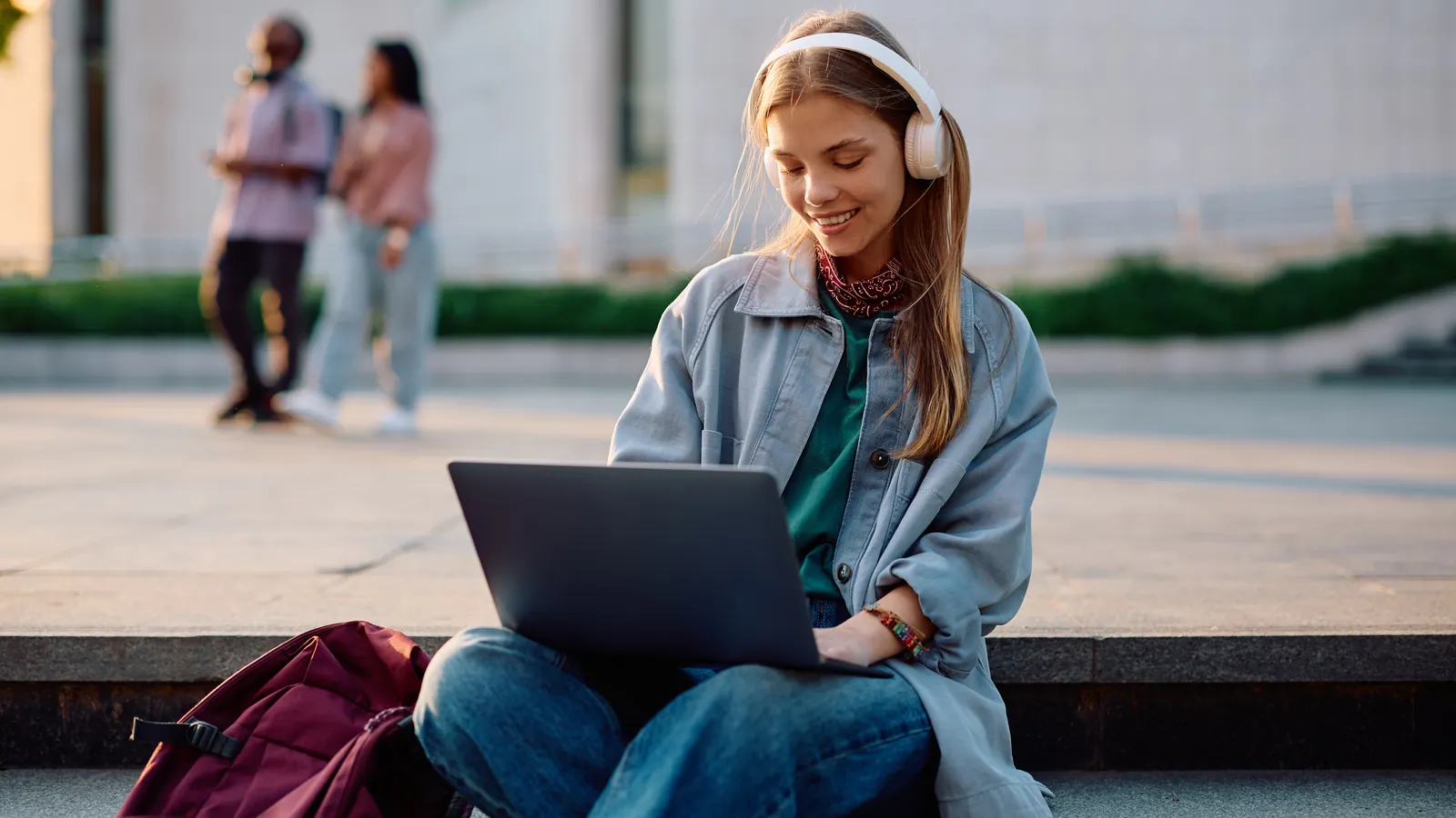 Étudiante avec un casque audio travaillant sur son ordinateur portable en plein air